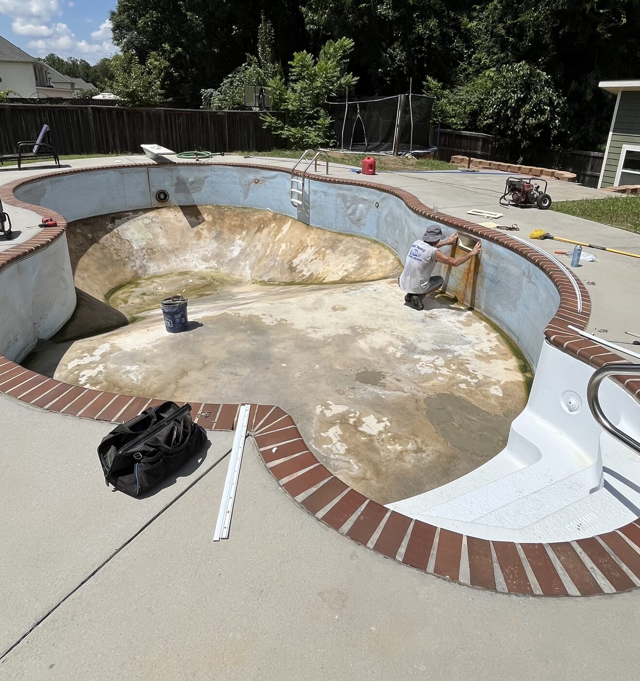 Freeform brick-coping pool drained with the old liner removed during replacement